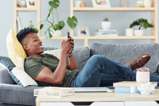 Shot of a young man using a cellphone while relaxing at home